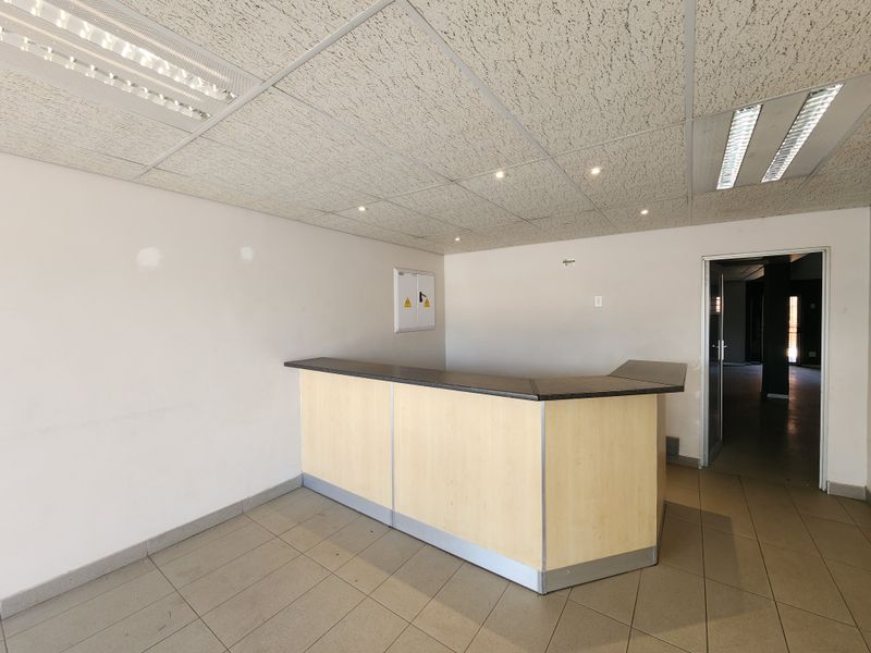 A vacant office space featuring a built-in reception desk, suspended ceiling with recessed lighting, and durable ceramic floor tiles.
