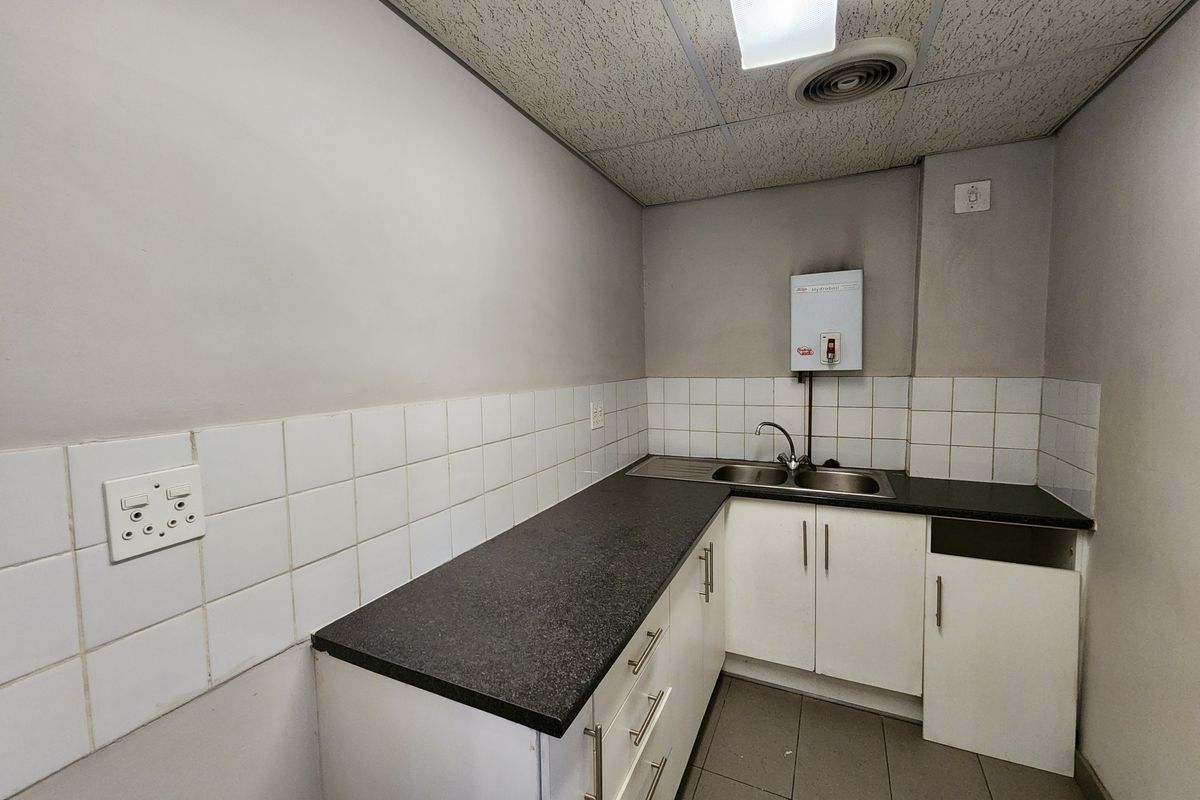 A compact industrial kitchenette featuring laminate countertops, stainless steel sink, tiled backsplash, and built-in cabinetry with a missing door panel.