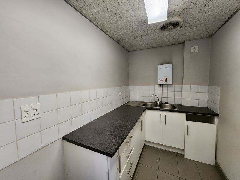 A compact industrial kitchenette featuring laminate countertops, stainless steel sink, tiled backsplash, and built-in cabinetry with a missing door panel.
