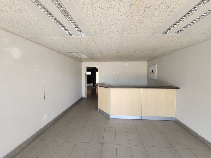 Empty office space featuring a built-in reception counter, tiled flooring, and suspended ceiling with recessed lighting.