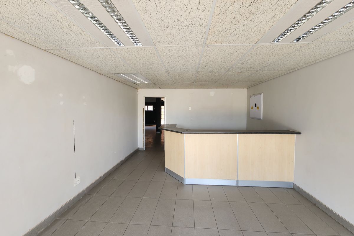 Empty office space featuring a built-in reception counter, tiled flooring, and suspended ceiling with recessed lighting.