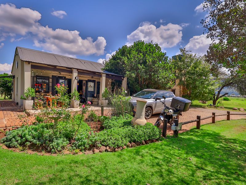 A charming industrial-style building featuring a corrugated metal roof, a covered patio area, and a well-maintained garden with brick paving.