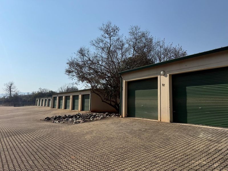 A row of industrial storage units featuring green roller shutter doors and a paved driveway area.