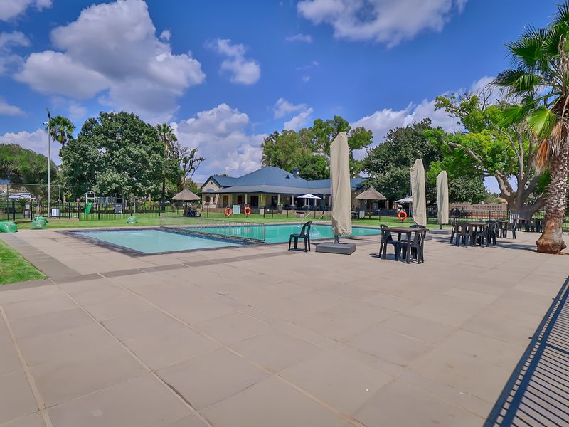 A well-maintained outdoor pool area featuring a paved deck, safety fencing, and landscaped surroundings, ideal for recreational use.