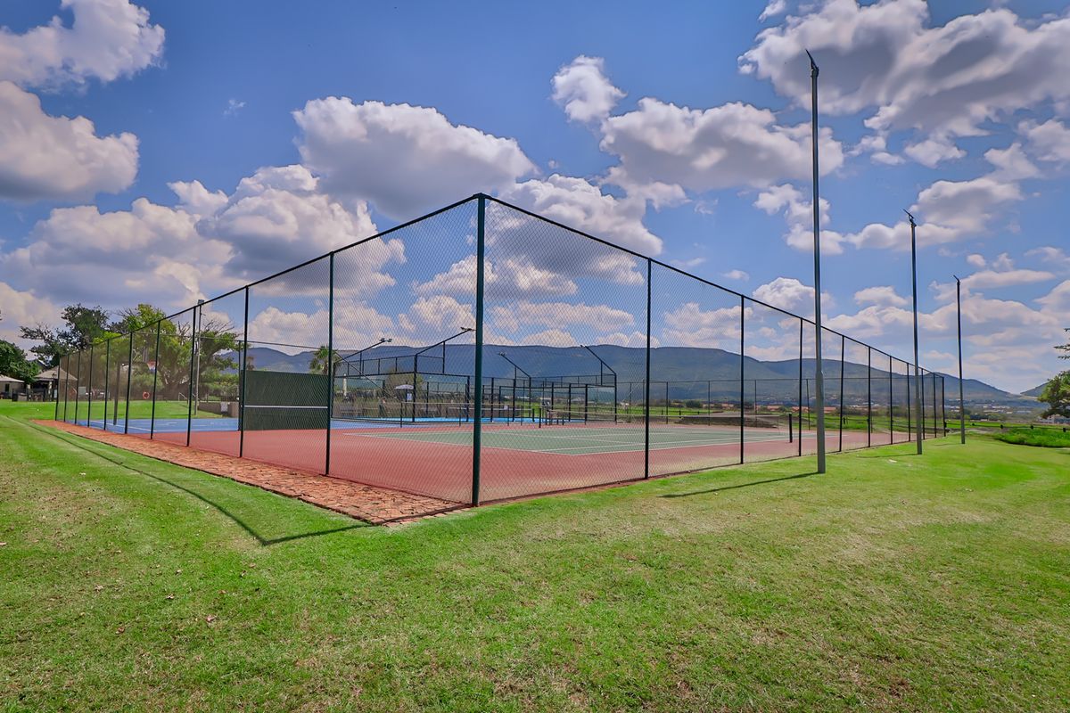 Well-maintained outdoor tennis court facility featuring perimeter fencing and integrated floodlighting, set within a landscaped estate environment.