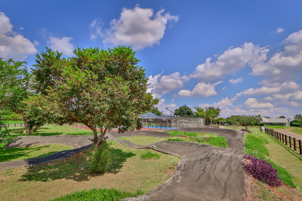 Outdoor recreational area featuring a paved pump track and a fenced sports court set within a landscaped estate environment.