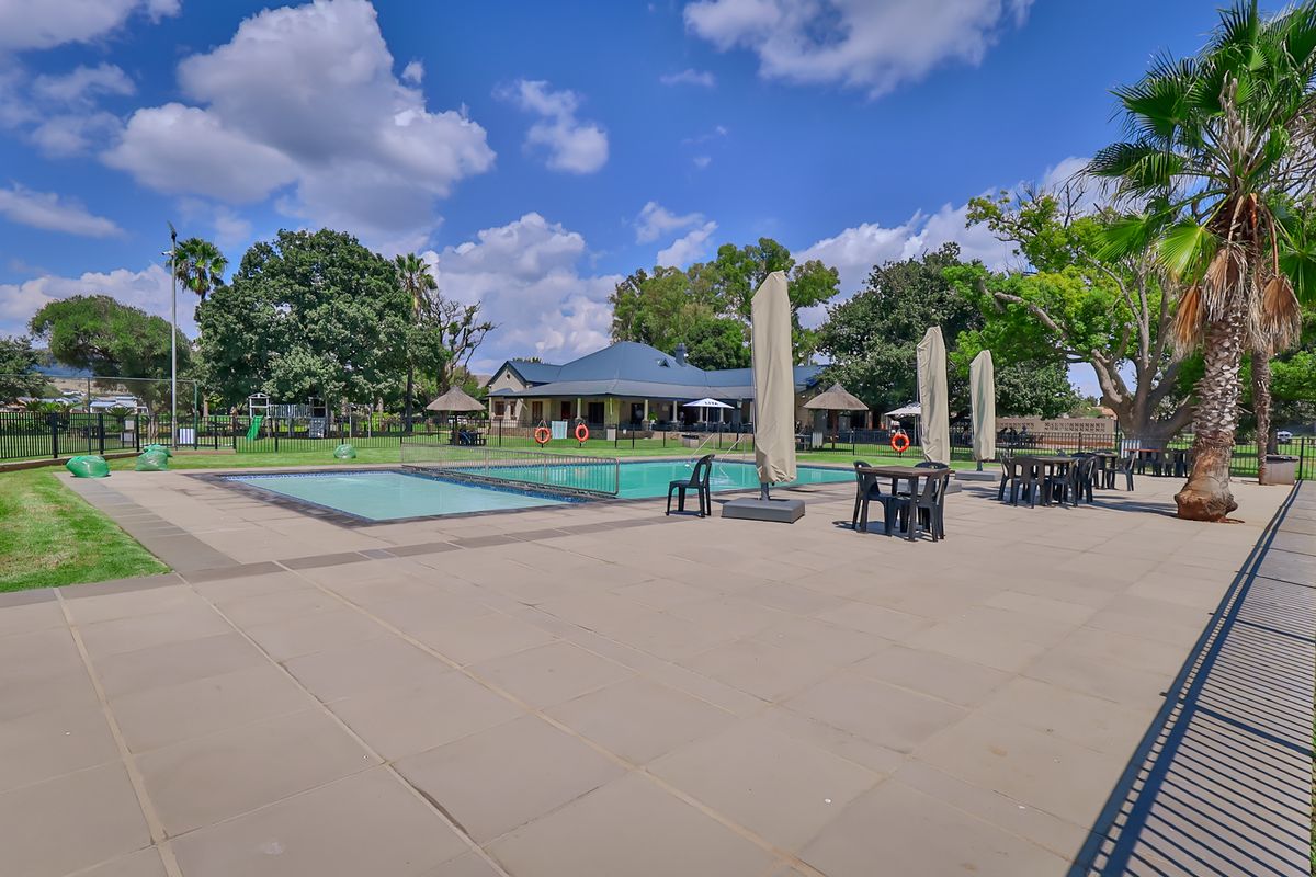 A well-maintained outdoor pool area featuring a paved deck, safety fencing, and landscaped surroundings, ideal for recreational use.