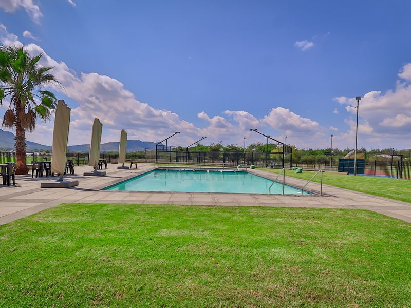 Outdoor swimming pool area featuring a paved deck, perimeter fencing, and integrated floodlighting, set within a well-maintained landscaped environment.