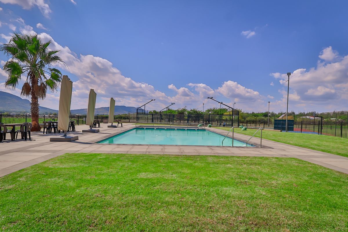 Outdoor swimming pool area featuring a paved deck, perimeter fencing, and integrated floodlighting, set within a well-maintained landscaped environment.
