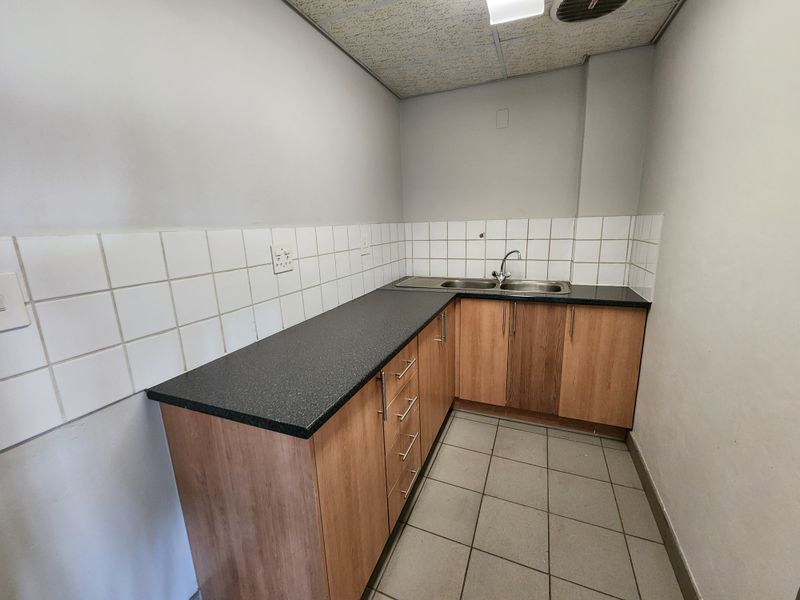 A functional scullery or kitchenette area featuring laminate cabinetry, a stainless steel double sink, tiled splashback, and durable tiled flooring.