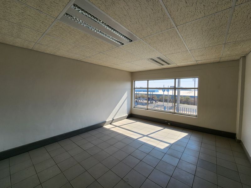 An empty, well-lit office space featuring tiled flooring, a suspended ceiling with recessed lighting, and a large window providing natural light.