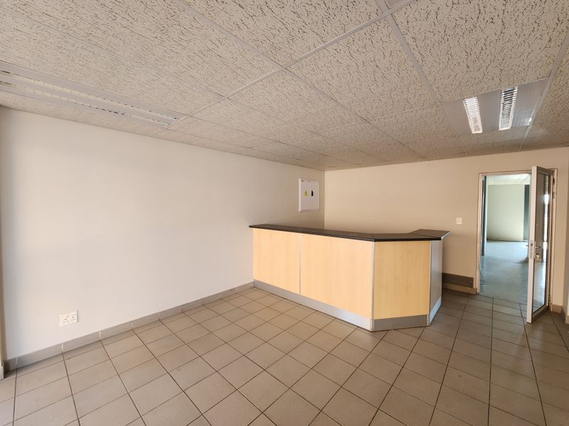 An empty office space featuring a built-in reception counter, tiled flooring, and suspended ceiling with recessed lighting.