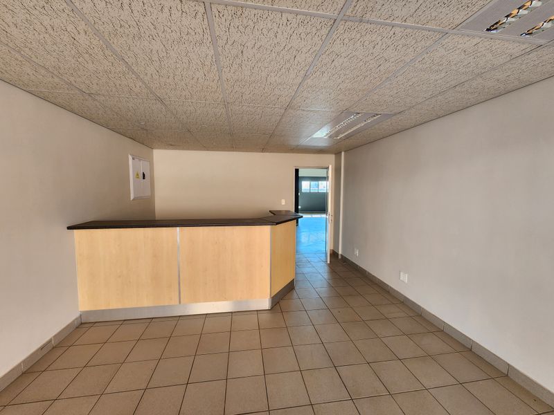An empty office space featuring a built-in reception counter, suspended ceiling tiles, and durable ceramic floor tiling, suitable for a professional workspace.