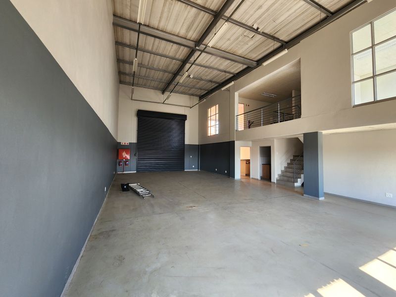 Spacious industrial warehouse unit featuring a high-clearance roller shutter door, concrete flooring, and a functional mezzanine level for additional office or storage space.