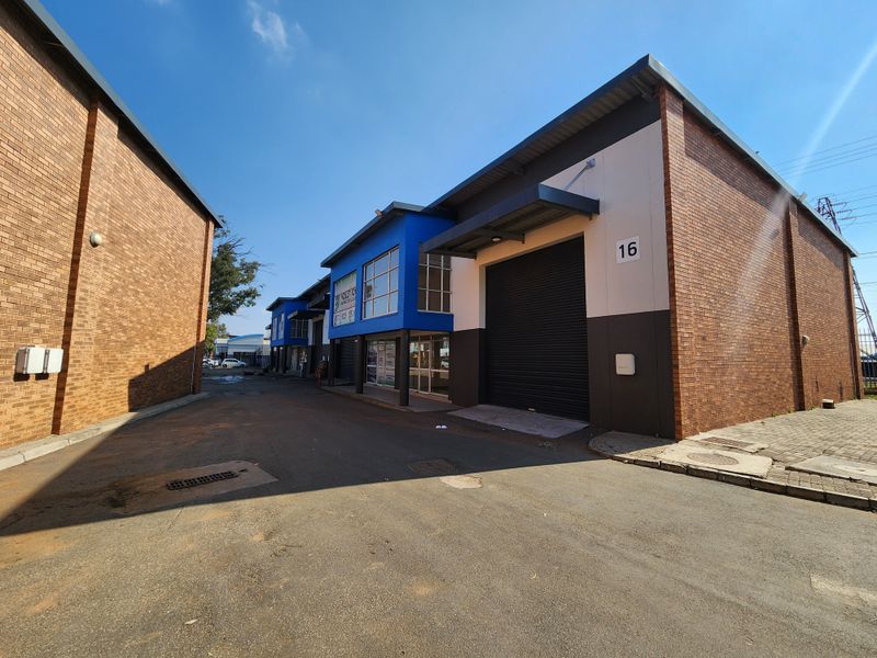 Exterior view of an industrial unit featuring a roller shutter door, brick facade, and paved driveway access within a commercial complex.