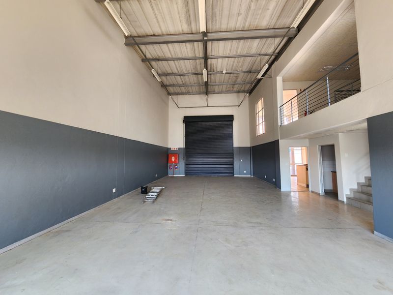Spacious industrial warehouse unit featuring high ceilings, a large roller shutter door, concrete flooring, and an integrated mezzanine level for additional storage or office space.