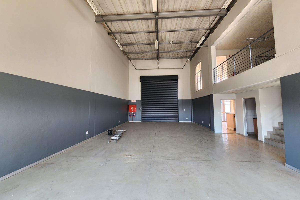 Spacious industrial warehouse unit featuring high ceilings, a large roller shutter door, concrete flooring, and an integrated mezzanine level for additional storage or office space.