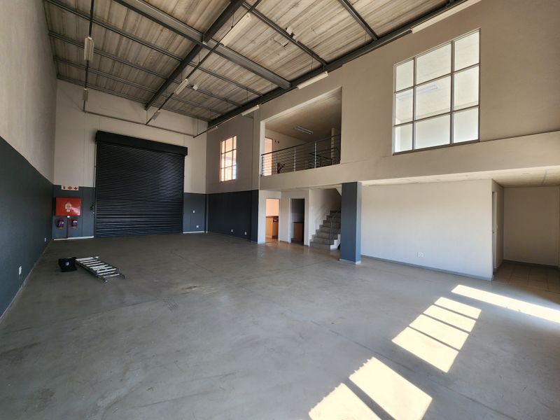 Spacious industrial warehouse unit featuring a high-clearance ceiling, roller shutter door, and a mezzanine level suitable for office or storage use.