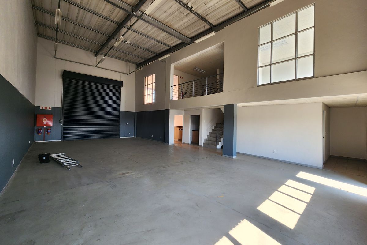 Spacious industrial warehouse unit featuring a high-clearance ceiling, roller shutter door, and a mezzanine level suitable for office or storage use.