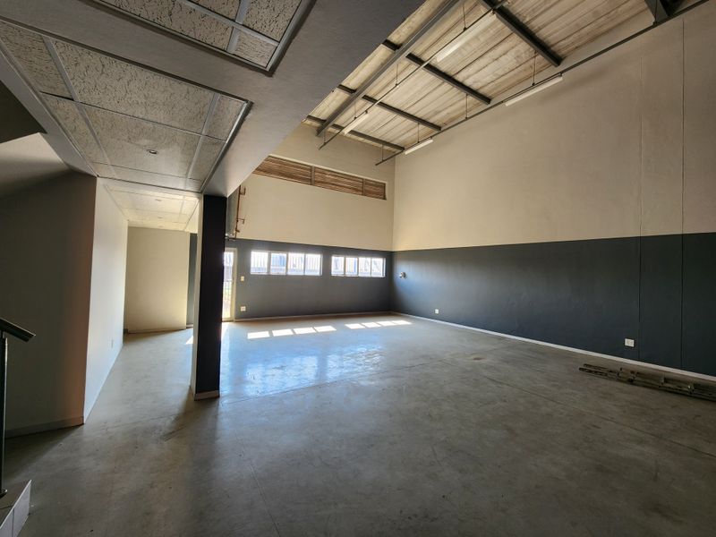 Spacious industrial utility area featuring high ceilings with exposed steel trusses, concrete flooring, and ample natural light from high-level windows.
