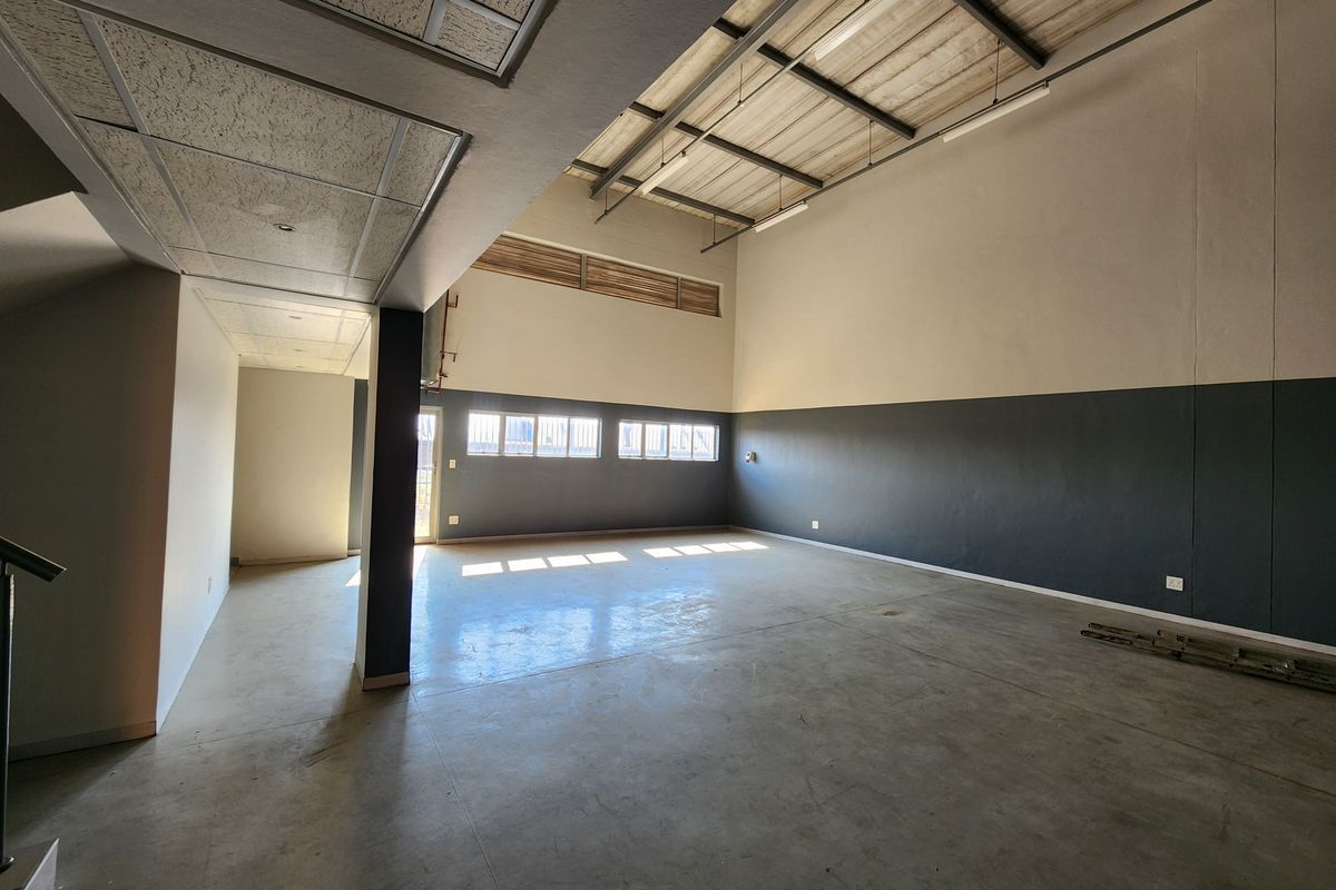 Spacious industrial utility area featuring high ceilings with exposed steel trusses, concrete flooring, and ample natural light from high-level windows.