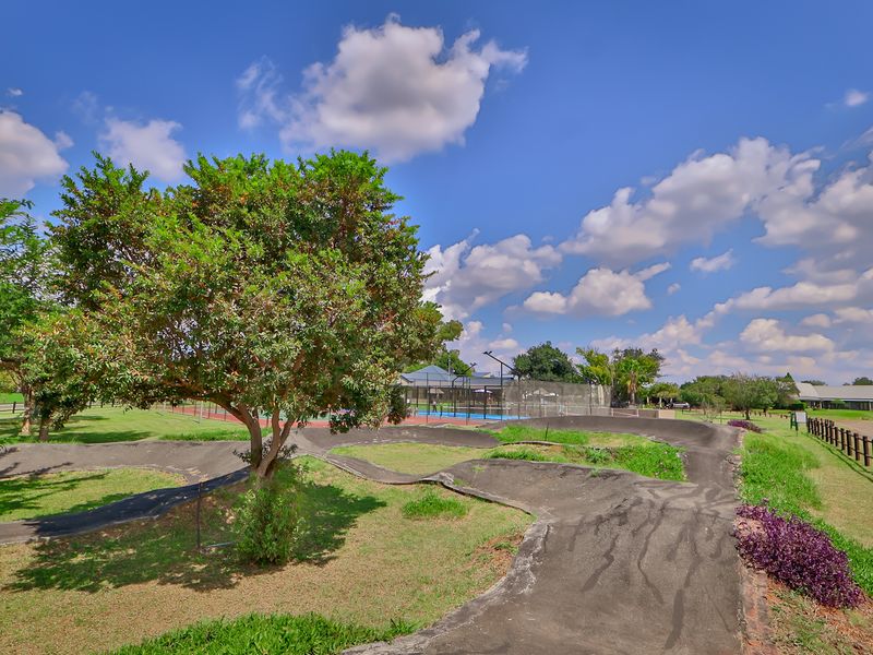 Outdoor recreational area featuring a paved pump track and a fenced sports court set within a landscaped estate environment.