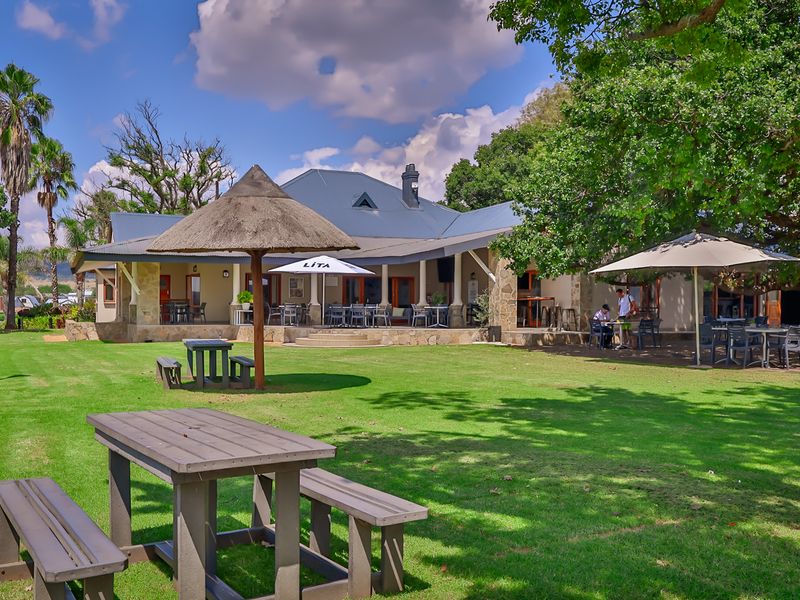 A well-maintained rear exterior view featuring a spacious lawn, a covered patio area with stone accents, and a traditional thatched gazebo.