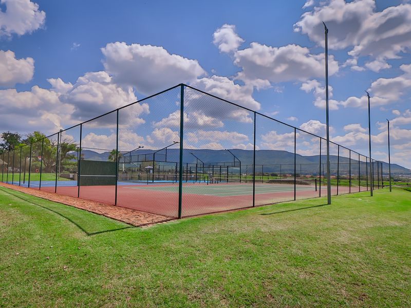 Well-maintained outdoor tennis court facility featuring perimeter fencing and integrated floodlighting, set within a landscaped estate environment.