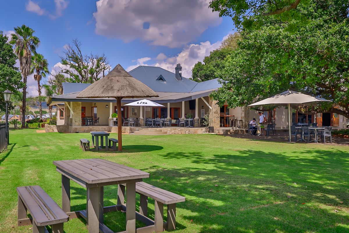 A well-maintained rear exterior view featuring a spacious lawn, a covered patio area with stone accents, and a traditional thatched gazebo.