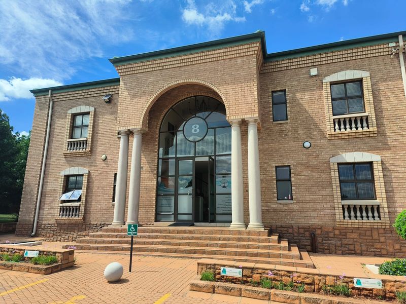 A professional front elevation of a brick office building featuring an arched entrance, decorative columns, and paved access with handicap parking.