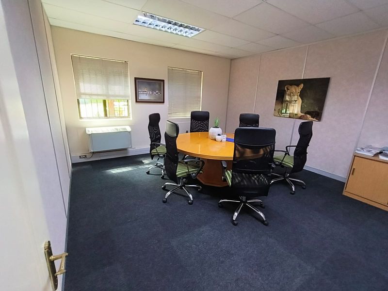 A functional office space featuring a suspended ceiling, recessed lighting, wall-mounted air conditioning, and carpeted flooring.