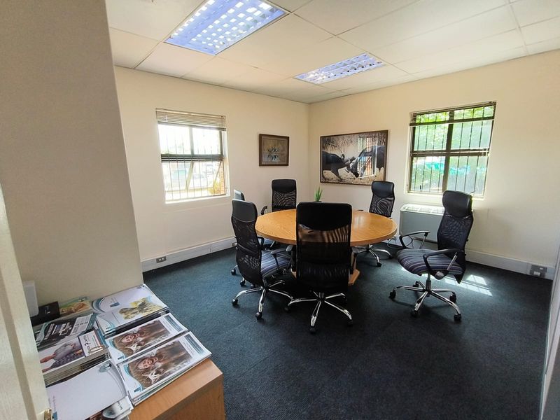 A functional office space featuring recessed lighting, carpeted flooring, and dual windows with security bars, providing a professional environment for meetings or workspace.