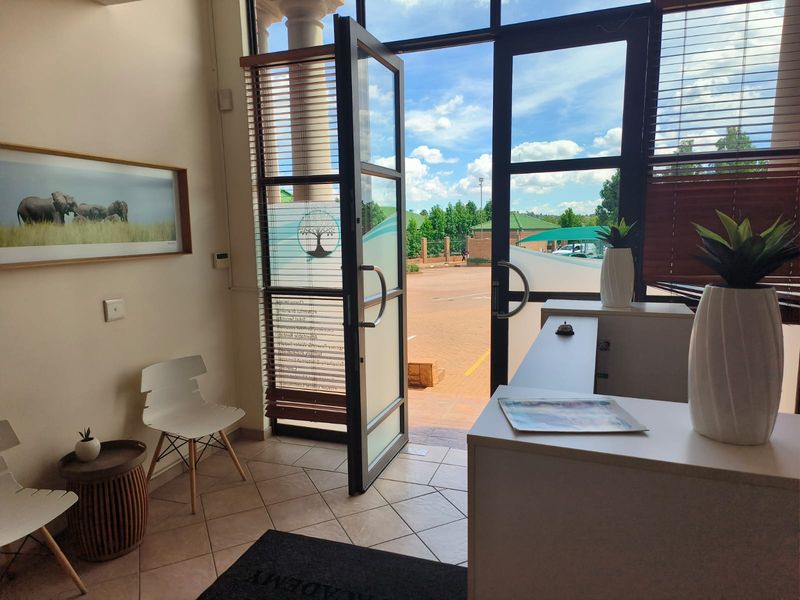 Bright office entrance area featuring a reception desk, tiled flooring, and large glass doors opening to the exterior parking area.