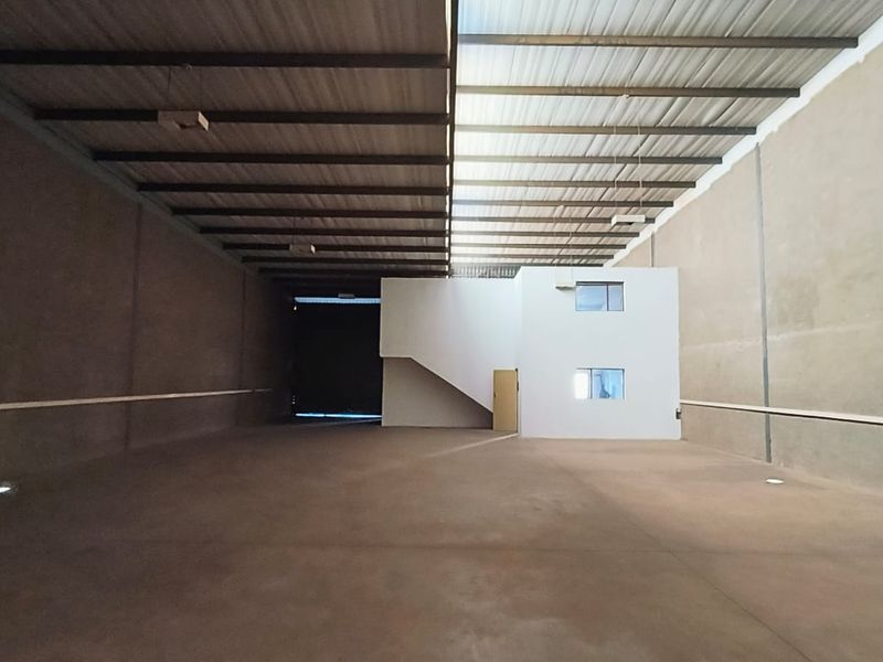 Spacious industrial warehouse unit featuring high ceilings with exposed steel trusses, concrete flooring, and a built-in internal office structure with stairs.