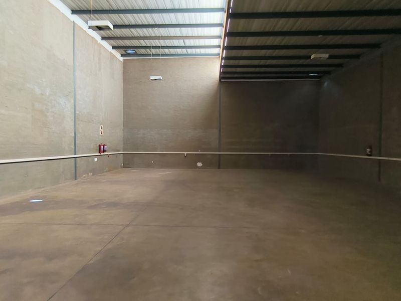Spacious industrial utility area featuring high ceilings with exposed steel trusses, concrete flooring, and natural light from a skylight.