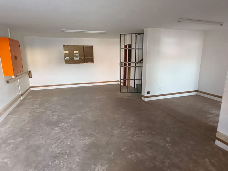 A functional industrial utility space featuring concrete flooring, a wall-mounted fire hose reel, electrical distribution board, and a secure metal gate.