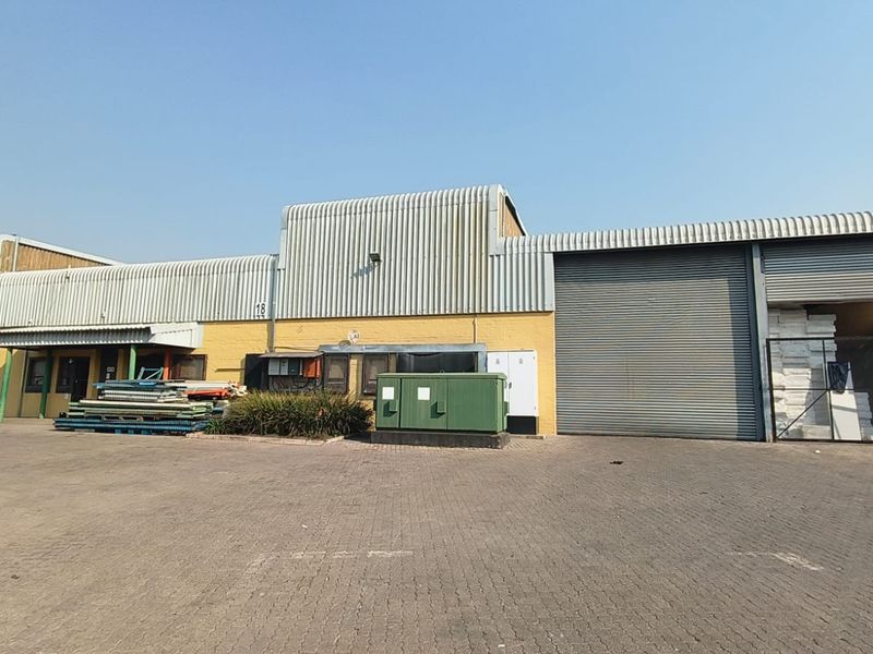 Industrial warehouse facility featuring corrugated metal cladding, roller shutter doors, and a paved yard area suitable for logistics or storage operations.