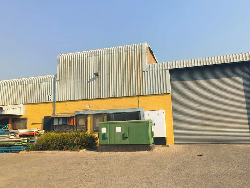 Industrial warehouse exterior featuring a large roller shutter door, corrugated metal cladding, and a paved yard area.