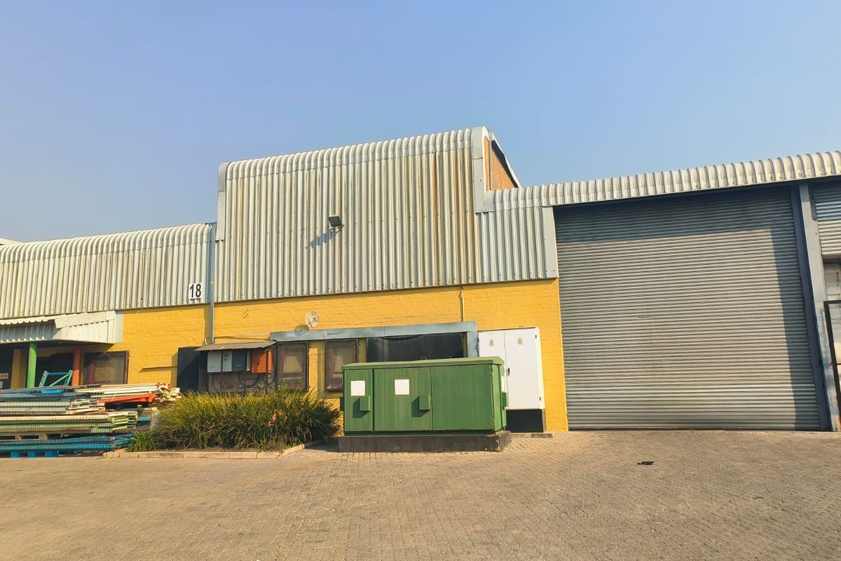 Industrial warehouse exterior featuring a large roller shutter door, corrugated metal cladding, and a paved yard area.