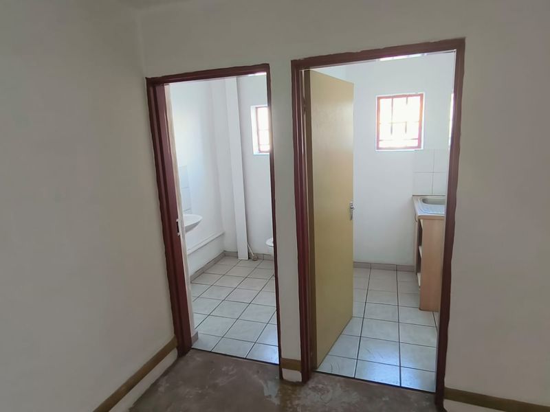 A view of a hallway leading into two separate bathroom or utility spaces, featuring tiled flooring and basic functional fixtures.