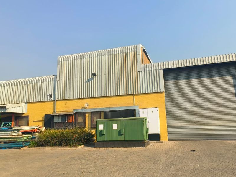 Industrial warehouse exterior featuring a large roller shutter door, corrugated metal cladding, and paved driveway access.