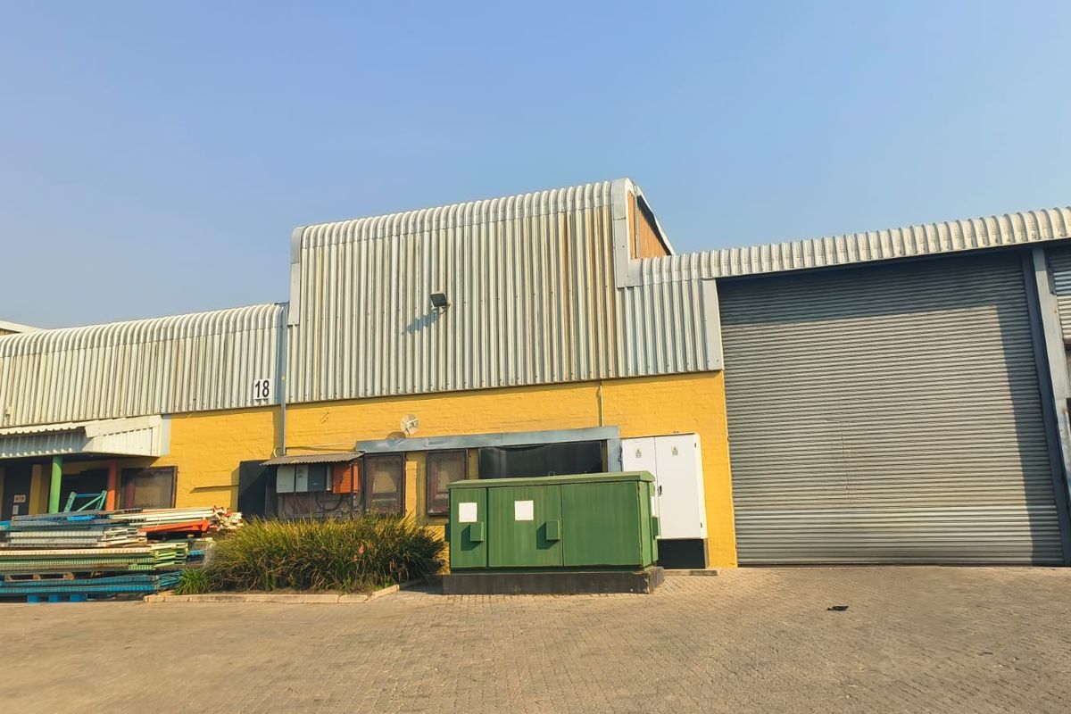 Industrial warehouse exterior featuring a large roller shutter door, corrugated metal cladding, and paved driveway access.