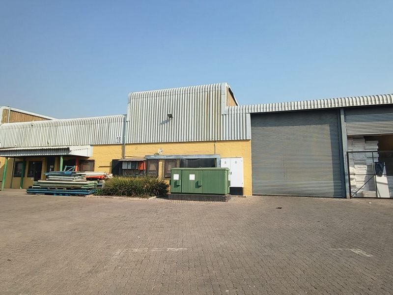 Industrial warehouse exterior featuring corrugated metal cladding, large roller shutter doors, and a paved yard area suitable for logistics or storage operations.