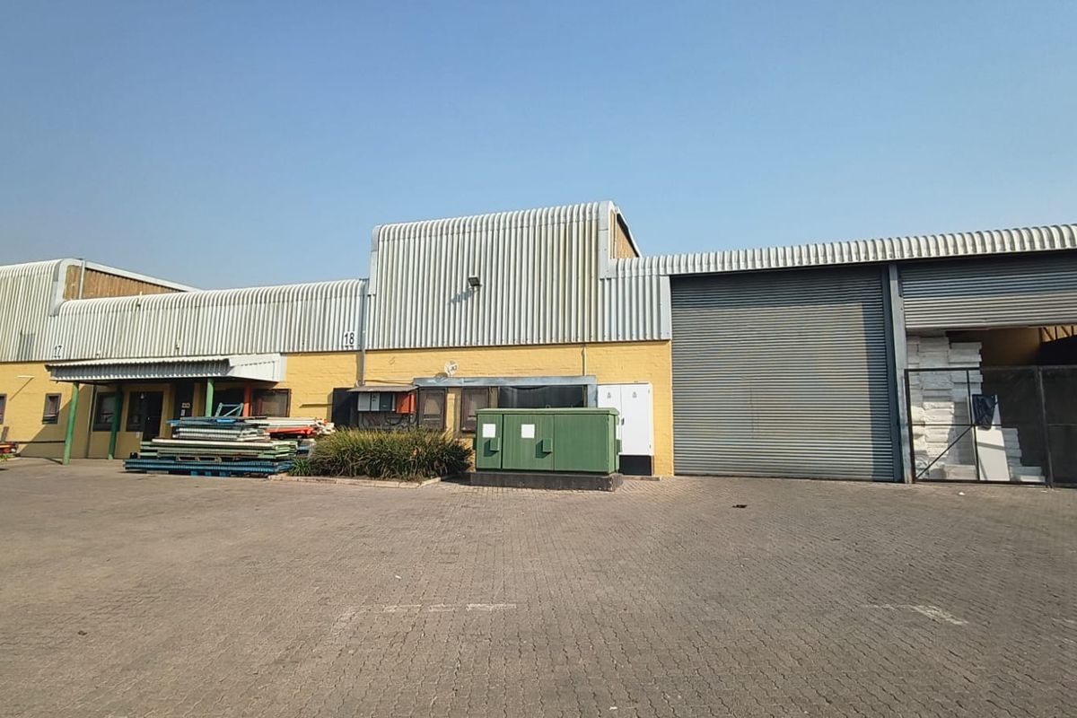 Industrial warehouse exterior featuring corrugated metal cladding, large roller shutter doors, and a paved yard area suitable for logistics or storage operations.