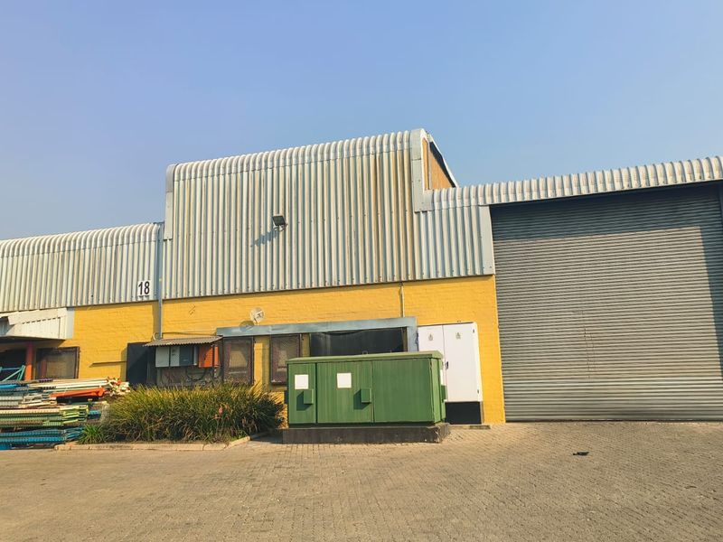 Industrial warehouse exterior featuring a large roller shutter door, corrugated metal cladding, and paved driveway access.