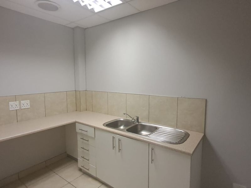 A clean and functional office scullery area featuring a double bowl stainless steel sink, laminate countertops, tiled splashback, and ample built-in cabinetry.