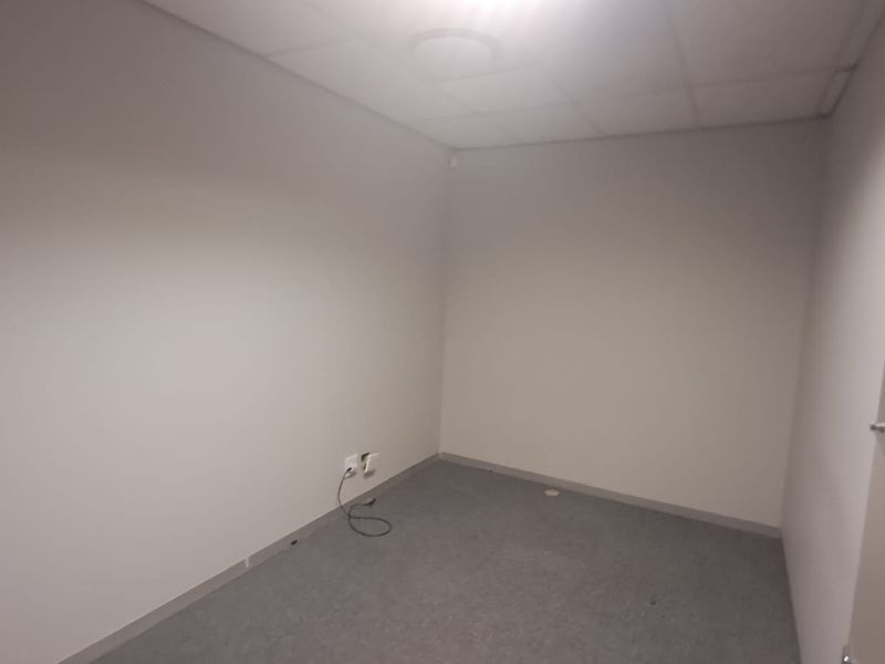 A vacant, neutral-toned office space featuring a suspended ceiling, carpeted flooring, and integrated electrical and data connectivity points.