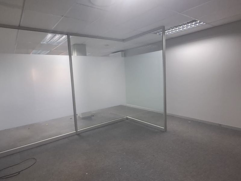 An empty office space featuring a glass partition, suspended ceiling with recessed lighting, and carpeted flooring.