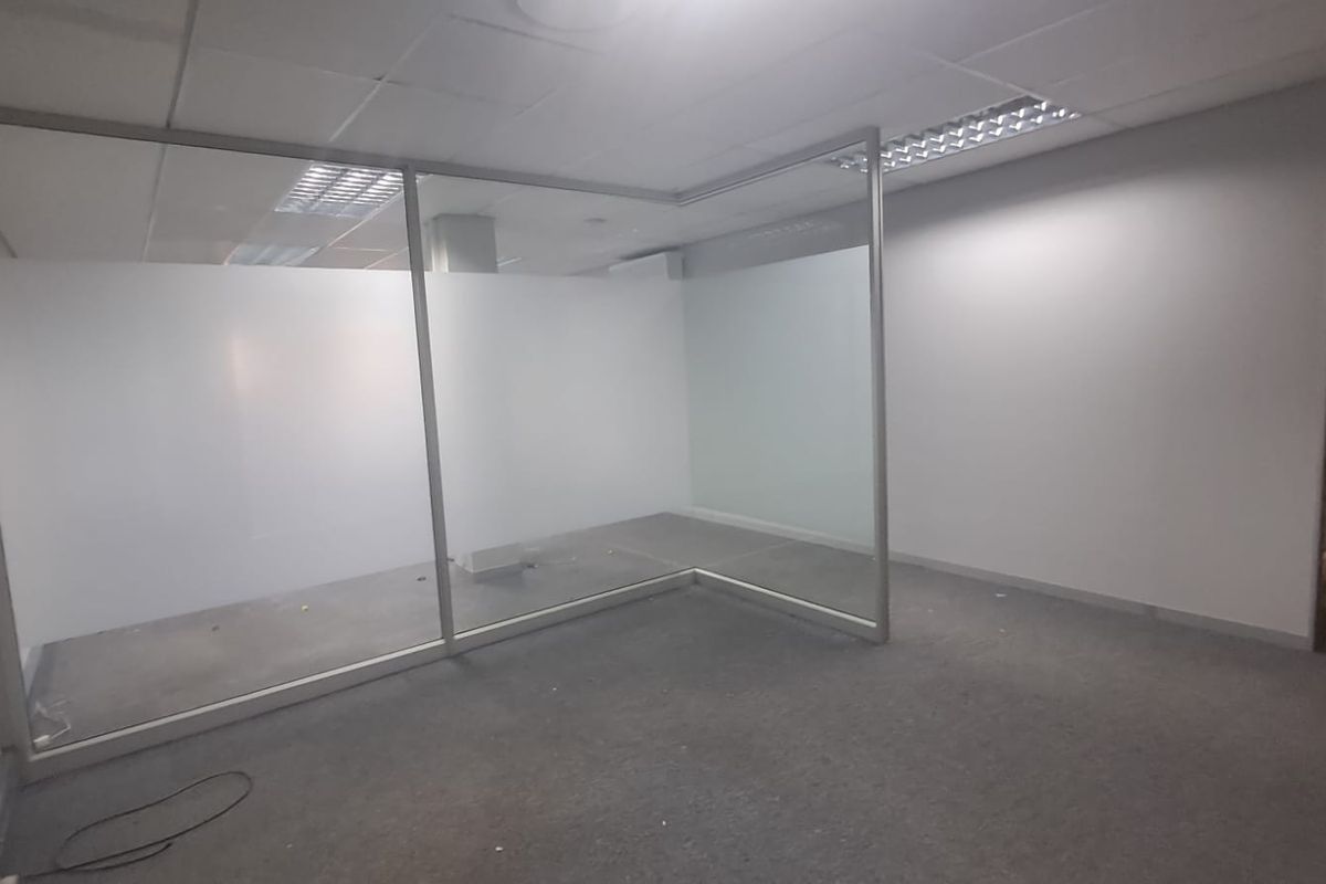 An empty office space featuring a glass partition, suspended ceiling with recessed lighting, and carpeted flooring.