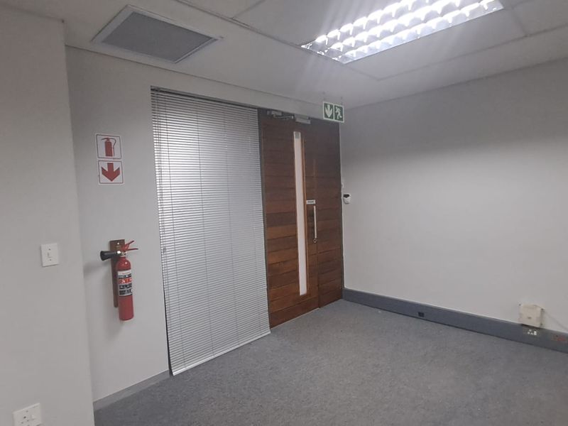 A vacant office space featuring carpeted flooring, a suspended ceiling with recessed lighting, and a solid timber entrance door.